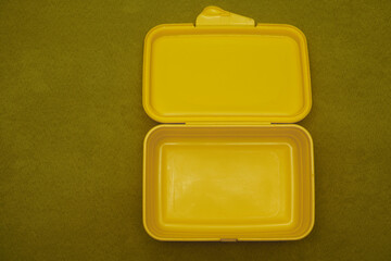 Yellow plastic tableware food container isolated over green background. empty  lunch box isolated. empty copy space. flat lay, top view.