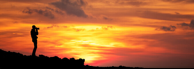 Wall Mural - banner of a sunset with a silhouette of a photographer in the act of photographing the landscape