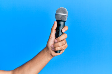 Hand of hispanic man holding microphone over isolated blue background.