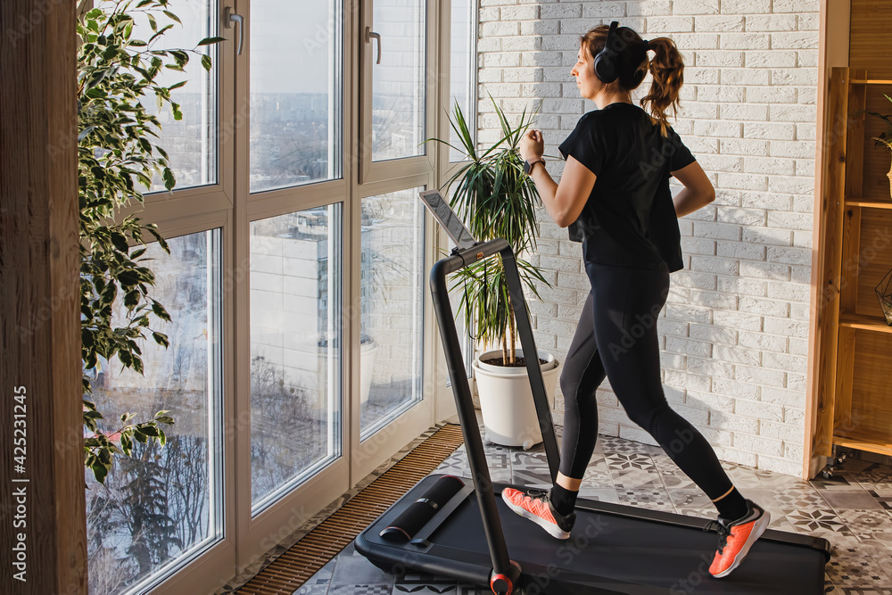 Woman jogging on the modern compact treadmill at home - obrazy, fototapety, plakaty 