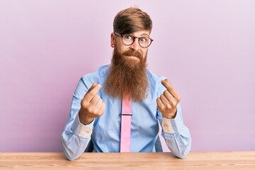 Canvas Print - Young irish redhead man wearing business shirt and tie sitting on the table doing money gesture with hands, asking for salary payment, millionaire business