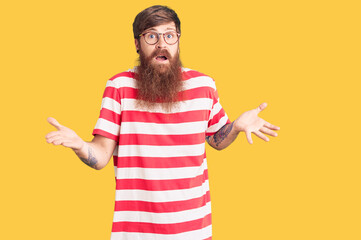 Sticker - Handsome young red head man with long beard wearing casual clothes clueless and confused expression with arms and hands raised. doubt concept.