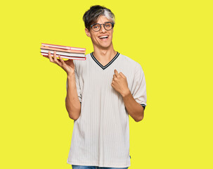 Wall Mural - Young hispanic man holding books pointing finger to one self smiling happy and proud