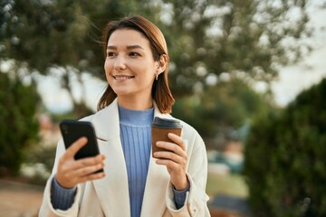 Young hispanic woman using smartphone and drinking coffee at the park.