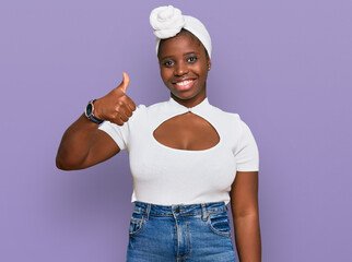 Wall Mural - Young african woman with turban wearing hair turban over isolated background doing happy thumbs up gesture with hand. approving expression looking at the camera showing success.