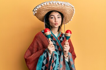 Poster - young caucasian woman holding mexican hat using maracas looking at the camera blowing a kiss being l