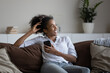 © fizkes - Smiling young African American woman sit relax on couch at home use modern smartphone gadget. Happy millennial biracial female have fun browsing internet on cellphone rest in living room on weekend.