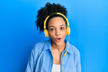 Sticker - Young african american girl listening to music using headphones scared and amazed with open mouth for surprise, disbelief face