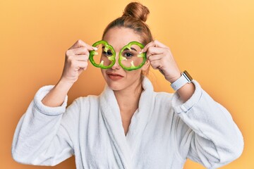 Canvas Print - Young blonde woman wearing bathrobe holding green pepper over eyes relaxed with serious expression on face. simple and natural looking at the camera.