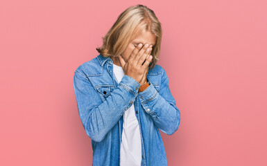 Poster - Caucasian man with blond long hair wearing casual denim jacket with sad expression covering face with hands while crying. depression concept.