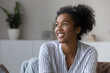 Smiling millennial African American woman relax in cozy own living room look in distance dreaming or visualizing. Happy young biracial female renter think or plan. Vision, visualization concept.