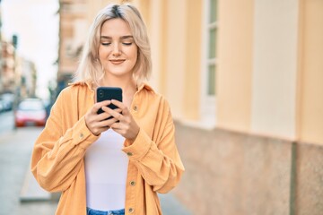 Sticker - Young blonde girl smiling happy using smartphone at the city.