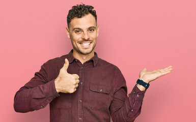 Young hispanic man wearing casual clothes showing palm hand and doing ok gesture with thumbs up, smiling happy and cheerful