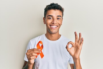 Young handsome african american man holding awareness orange ribbon doing ok sign with fingers, smiling friendly gesturing excellent symbol