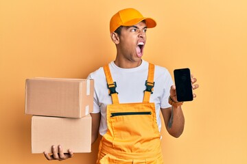 Sticker - Young handsome african american man holding delivery package and showing smartphone screen angry and mad screaming frustrated and furious, shouting with anger. rage and aggressive concept.