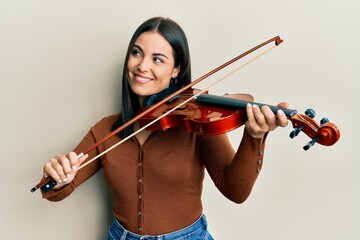 Young brunette woman playing violin smiling looking to the side and staring away thinking.