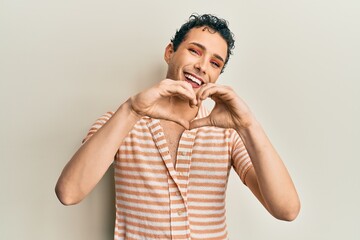 Handsome man wearing make up wearing casual t shirt smiling in love doing heart symbol shape with hands. romantic concept.