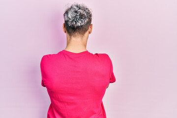 Young hispanic man with modern dyed hair wearing casual pink t shirt standing backwards looking away with crossed arms