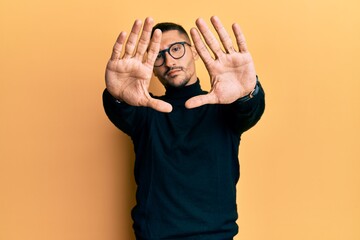 Poster - Handsome man with tattoos wearing turtleneck sweater and glasses doing frame using hands palms and fingers, camera perspective