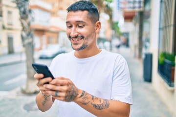 Poster - Young hispanic man smiling happy using smartphone at street of city.