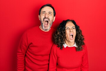 Poster - Middle age couple of hispanic woman and man hugging and standing together angry and mad screaming frustrated and furious, shouting with anger. rage and aggressive concept.