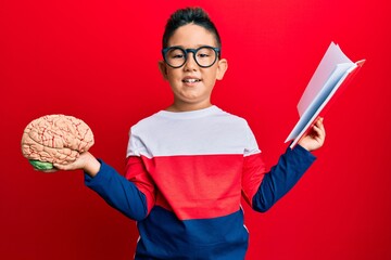 Sticker - Little boy hispanic kid holding brain studying for school smiling with a happy and cool smile on face. showing teeth.