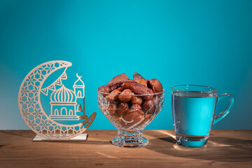 Wall Mural - Muslim iftar of breaking of fast during Ramadan month with preserved sweet dates and water. Decorative crescent and mosque as prop