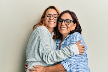 Hispanic mother and daughter smiling happy and hugging standing over isolated white background.