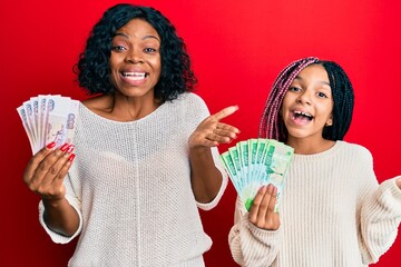 Poster - Beautiful african american mother and daughter holding russian ruble banknotes celebrating achievement with happy smile and winner expression with raised hand