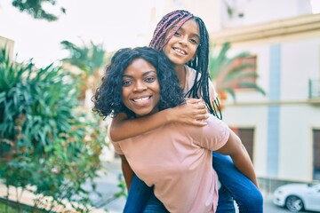 Poster - Beautiful african american mother giving daughter piggyback ride smiling happy at the park.