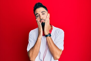 Poster - Young man with beard listening to music using headphones tired hands covering face, depression and sadness, upset and irritated for problem