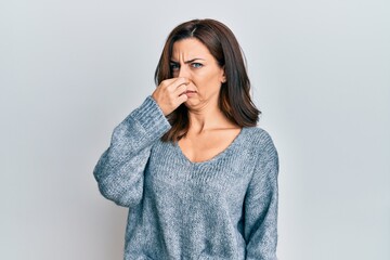 Canvas Print - Young brunette woman wearing casual winter sweater smelling something stinky and disgusting, intolerable smell, holding breath with fingers on nose. bad smell