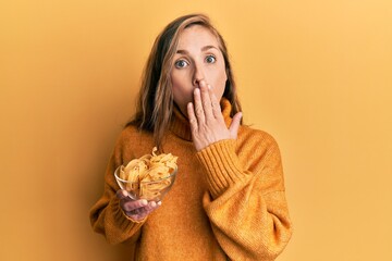 Wall Mural - Young blonde woman holding bowl with uncooked pasta covering mouth with hand, shocked and afraid for mistake. surprised expression