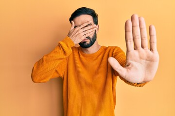 Wall Mural - Young hispanic man wearing casual clothes covering eyes with hands and doing stop gesture with sad and fear expression. embarrassed and negative concept.