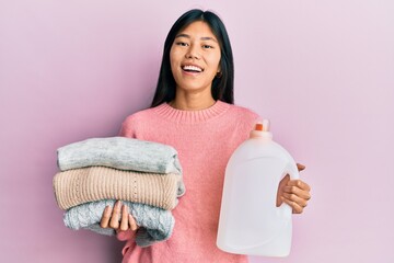 Sticker - Young chinese woman holding detergent bottle and clothes smiling and laughing hard out loud because funny crazy joke.