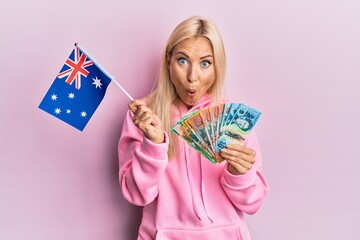 Sticker - Young blonde woman holding australian flag and dollars afraid and shocked with surprise and amazed expression, fear and excited face.