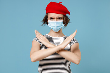 Wall Mural - Young woman 20s wear french beret red hat striped t-shirt sterile mask coronavirus covid-19 pandemic quarantine do stop gesture crossed hands folded isolated on pastel blue background studio portrait.