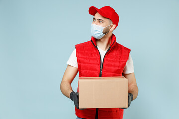 Wall Mural - Delivery guy employee man in red cap white t-shirt vest uniform sterile face mask gloves work courier service on lockdown covid19 flu virus hold empty cardboard box isolated on pastel blue background