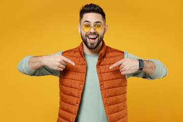 Wall Mural - Young surprised shocked amazed excited happy fun impressed man 20s years old wearing orange vest mint sweatshirt glasses point index finger on himself isolated on yellow background studio portrait
