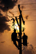 The silhouette of power lineman climbing on an electric pole with a transformer installed. And replacing the damaged hotline clamp, bail clamp, dropout and surge arrester that causes a power failure.