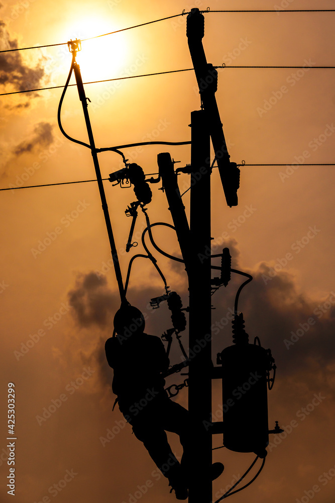 The silhouette of power lineman climbing on an electric pole with a ...