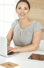 Wall Mural - Cheerful smiling businesswoman working with laptop computer while sitting at the desk in modern office. Middle aged female lawyer or auditor at work. Business people concept