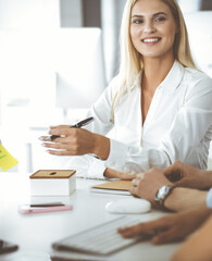 Wall Mural - Group of business people discussing questions at meeting. Headshot of blonde businesswoman while smiling to her colleague at office negotiation. Teamwork and cooperation in corporate occupation