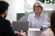 © fizkes - Confident middle-aged Caucasian businesswoman talk with colleagues or clients at office meeting. Successful mature female leader or boss lead head briefing with business partners. Leadership concept.