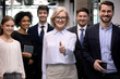 © fizkes - Portrait of smiling middle-aged businesswoman stand forefront of multiracial staff show thumb up give recommendation. Diverse multiethnic businesspeople recommend good quality company service.