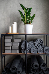 the interior of the room is a studio for sports yoga or stretching. table rack with accessories for classes - gray support cubes, rubber mats and plaids. decor candles and zamioculcas zamiifolia plant