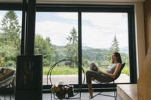 Beautiful Stylish Woman Reading Book, Sitting On Chair At Fireplace On Background Of Mountain Hills