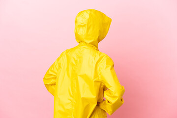 Young latin woman wearing a rainproof coat over isolated background in back position and looking side