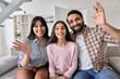 © insta_photos - Happy indian couple and teen child daughter waving hands looking at camera sitting on couch at home. Cheerful family having video call virtual meeting greeting in online chat, webcam view portrait.