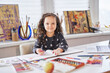 © boytsov - Cute child girl sitting at the table in headphones doing homework drawing using pencils or crayons. Homeschooling during coronavirus covid-19 or online art class concept. High quality photo